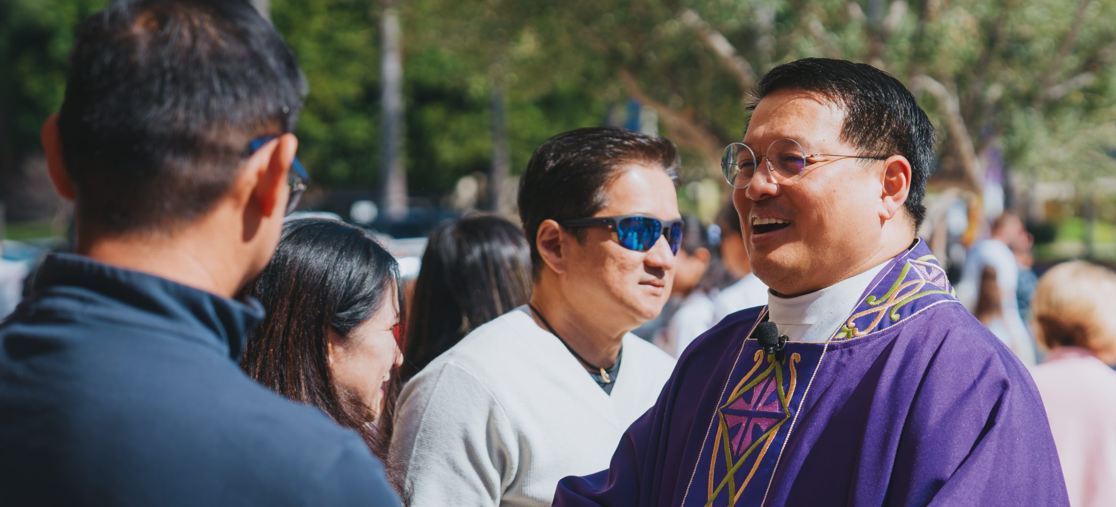 A priest in violet vestments greeting parishioners outside church after Mass